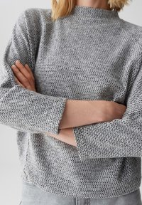 Grijze gebreide trui met een gestructureerd patroon, hoge halslijn en cropped mouwen. Het materiaal lijkt zacht en iets rekbaar.