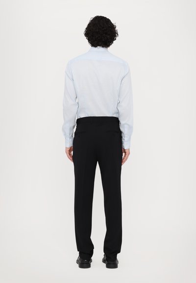 Chemise bleu clair à manches longues et pantalon noir ajusté. La chemise a une texture lisse ; le pantalon présente une coupe traditionnelle et des poches discrètes.