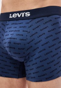 Μπλε ναυτικό σλιπ boxer της Levi's με επαναλαμβανόμενο λογότυπο, φορεμένο από άτομο και με φαρδύ ελαστικό κορδόνι με το εμπορικό σήμα.