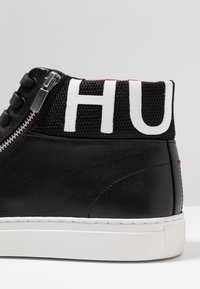 Black leather high-top sneaker with a mesh collar featuring "HU" in white. Silver zipper on the side and white rubber sole.