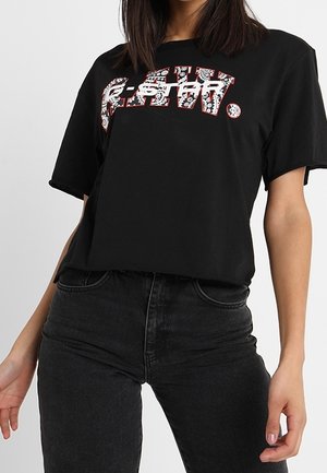 Zwart T-shirt met korte mouwen en een gedurfde, gemêleerde print in rood en wit over de borst. Losse pasvorm, gemaakt van zacht katoen.