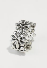 Bague en métal argenté présentant un motif floral avec des pétales arrondis et des centres évidés, créant une apparence texturée et complexe.