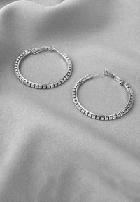 Silberne Creolen mit kleinen, rechteckigen Akzenten, die gleichmäßig am äußeren Rand verteilt sind, und einem sicheren Verschluss.