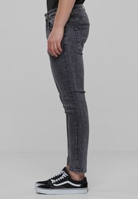 Slim fit fekete vászonfarmerek, kopott részletekkel, öt zsebes dizájnnal és gombos záródással. Fekete és fehér tornacipővel párosítva.