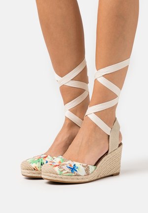 Chaussures espadrilles compensées avec tige en tissu floral, détails en toile beige et liens croisés à la cheville. Talon compensé en jute naturel.