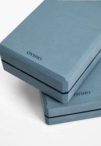 Des boîtes rectangulaires bleues avec une surface texturée et une bande d'accent noire. Le dessus présente le nom de la marque "OYSHO" imprimé en noir.