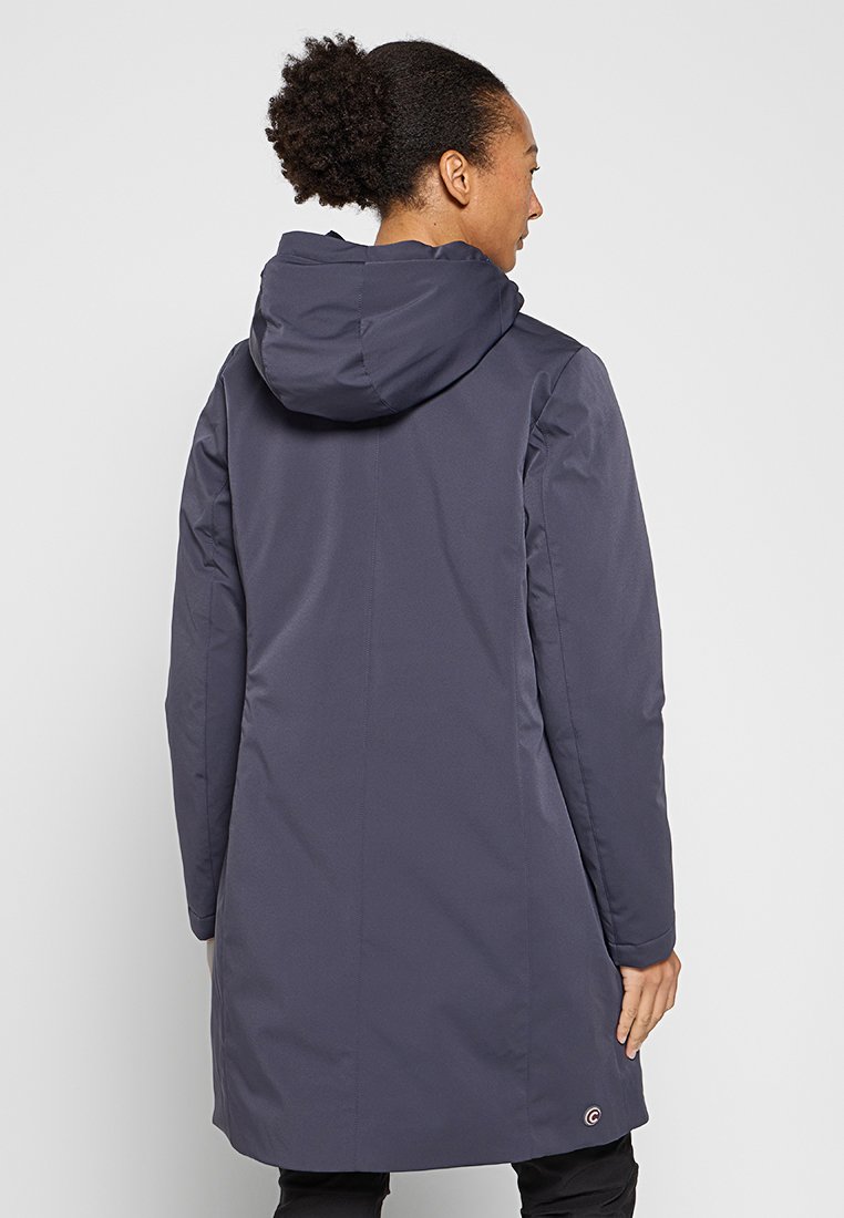 Marinblå vattentät jacka med en huva, rak silhuett, slät textur och logodetalj vid nederkant, designad för optimal täckning.