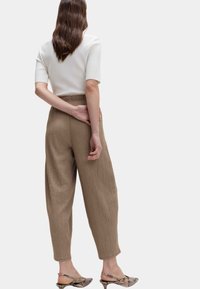 White ribbed short-sleeve top paired with light brown textured wide-leg trousers and patterned heeled mules, viewed from behind.