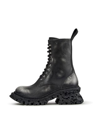 Botte de combat en cuir noir avec semelle épaisse texturée et lacets à l’avant, avec une languette à l’arrière.