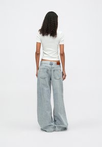 Άσπρο κοντομάνικο t-shirt συνδυασμένο με χαλαρές, ανοιχτόχρωμες μπλε φαρδιές παντελόνες. Σημαντικές λεπτομέρειες περιλαμβάνουν μια καφέ δερμάτινη ετικέτα στην πλάτη της ζώνης.