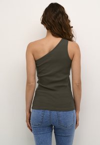 Olivově zelený top na jedno rameno s ribbed texturou. Přiléhavý střih, zkombinovaný s vysokými modrými džíny v klasickém džínovém stylu.