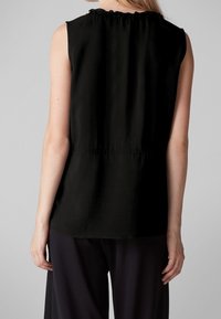 Top negro sin mangas con escote fruncido y cintura ceñida, con una textura suave y corte recto, acompañado de pantalones oscuros.