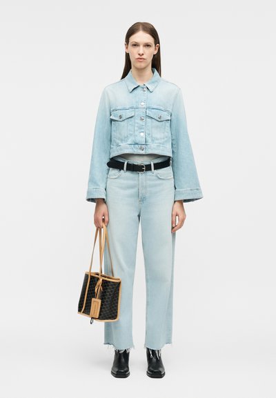 Γυναίκα που φοράει κοντό τζιν μπουφάν ανοιχτού μπλε χρώματος και τζιν παντελόνι στο ίδιο χρώμα, μαύρη ζώνη, μαύρες μπότες, κρατώντας μια μαύρη τσάντα με καρό σχέδιο και ταμπά περιμετρική κορδέλα.