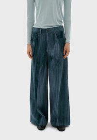 Pantalones de mezclilla de pierna ancha en azul oscuro con un acabado texturizado, que cuentan con bolsillos frontales y un cierre de botón en la cintura.