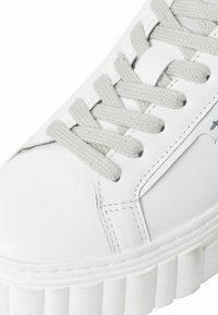 Baskets blanches avec une tige en cuir épurée, lacets gris, détails de couture subtils, et une semelle en caoutchouc texturée dotée de rainures verticales.