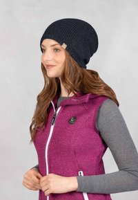 Zwarte gebreide beanie met een textuurpatroon, met een klein logotag. Gecombineerd met een paarse vest en een grijze langslijfs T-shirt.