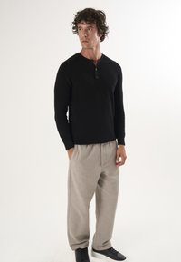 Schwarz geripptes Langarm-Henley-Shirt mit Knopfleiste, kombiniert mit hellbeigen, lässigen Hosen und schwarzen Sneakers.