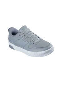 Zapatilla deportiva gris claro con parte superior sintética lisa, suela de goma prominente y cordones tonales. Presenta detalles de logotipos en los lados y la lengüeta.