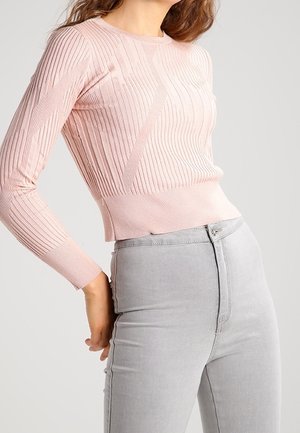 Lichtroze ribbel trui met lange mouwen, een ronde halslijn en een getailleerde pasvorm, gecombineerd met grijze high-waisted jeans.