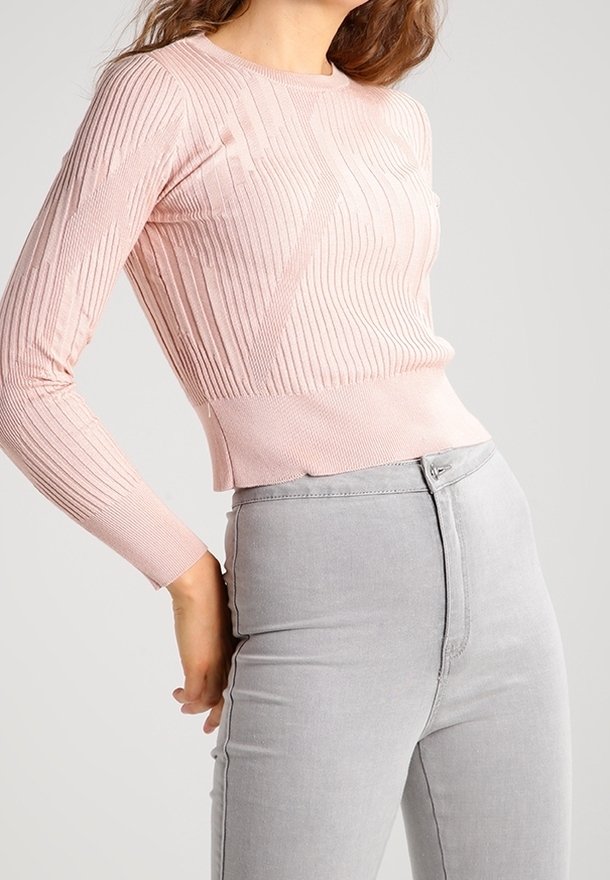 Ljusrosa ribbad stickad tröja med lång ärm, rund halsringning och en figurnära silhuett, i kombination med grå högmidjade jeans.