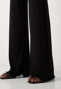 Sorte vid benbukser laget av strukturert stoff med en hemline som har en subtil scallop. Kombinert med svarte slidesandaler.
