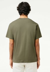 T-shirt in cotone verde oliva con maniche corte, vestibilità casual, scollatura rotonda e orlo dritto, caratterizzato da una texture liscia e un design minimale.