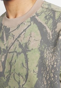 Felpa grigia chiara caratterizzata da un motivo camouflage con elementi verdi e marroni, realizzata in tessuto di cotone testurizzato e con collo a costine.