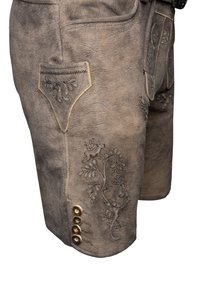 Braune Lederhosen mit dekorativer Stickerei, einer Vorderasche und vier dekorativen Knöpfen an der Seite. Strukturierte Oberfläche mit natürlicher Abnutzung.