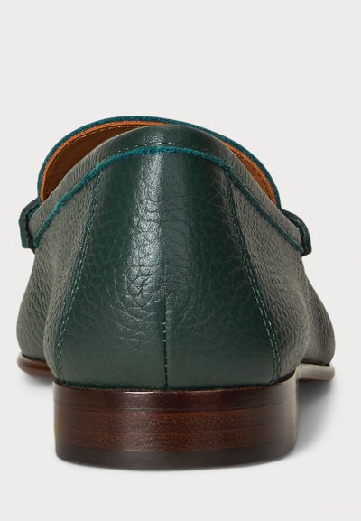 Mocassins de couro verde escuro com um acabamento texturizado. Apresentam uma sola de madeira castanha e costura contrastante ao longo da borda. Design clássico.