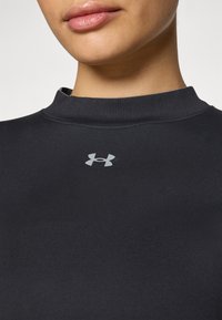 Črn dolg rokav športni top z visokim ovratnikom, narejen iz gladkega blaga. Ima majhen srebrni logotip Under Armour na prsih.