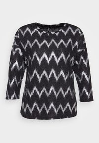 Svart långärmad tröja med vit zigzag-mönster och rund halsringning, visad på en enkel ljus bakgrund.