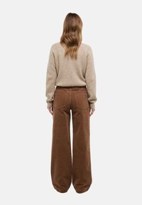 Pantalon large en velours côtelé marron avec poches arrière et finition texturée, associé à un pull en maille beige, vu de dos.