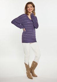Maglione viola lavorato a maglia con scollatura a V, motivi texturizzati e maniche lunghe. Abbinato a pantaloni bianchi e stivali da cowboy beige.