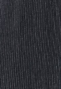 Gros plan sur un tissu noir avec de fines rayures verticales en paillettes argentées formant un motif texturé et scintillant.