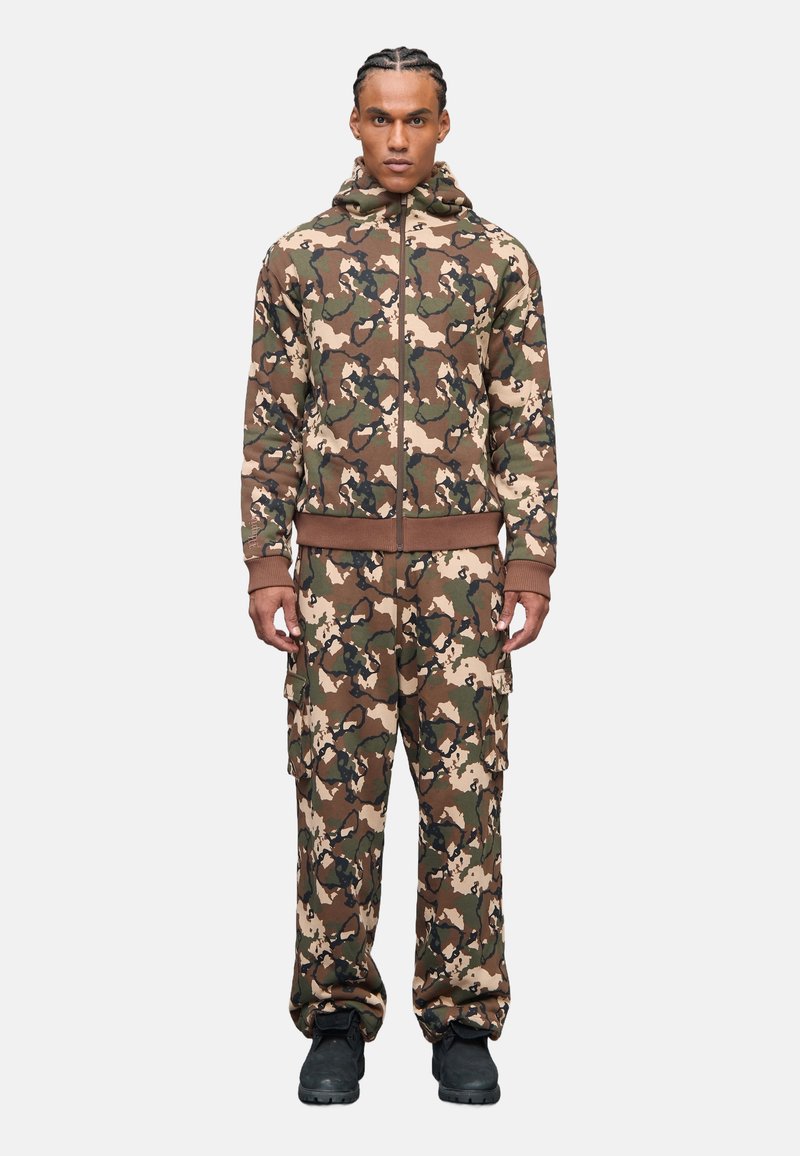 Camojas en cargobroekset in bruin, groen en beige. Met ritssluiting aan de voorkant en capuchon. Materiaal lijkt zacht en heeft voldoende zakken.