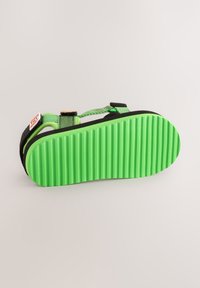 Žalios gumos pado su horizontaliomis grioveliais, juodos viršutinės dirželiai ir šoninė etiketė. Yra reguliuojami dirželiai, užtikrinantys patogų prisitaikymą.