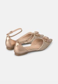 Chaussures plates dorées avec un dessus en paillettes scintillantes, bout pointu et accents de gemmes décoratives à l'avant, dotées d'une sangle ajustable à la cheville.