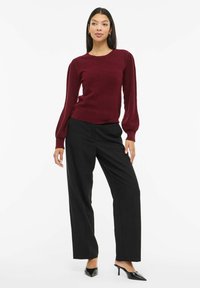 Bordowy sweter z teksturowanym splotem z bufkami, zestawiony z czarnymi szerokimi spodniami i czarnymi szpilkami z zaostrzonym noskiem.