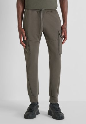 Olivengroene cargo pants met een taps toelopend ontwerp, een elastische tailleband met trekkoord en twee zijzakken. Gecombineerd met zwarte sneakers.