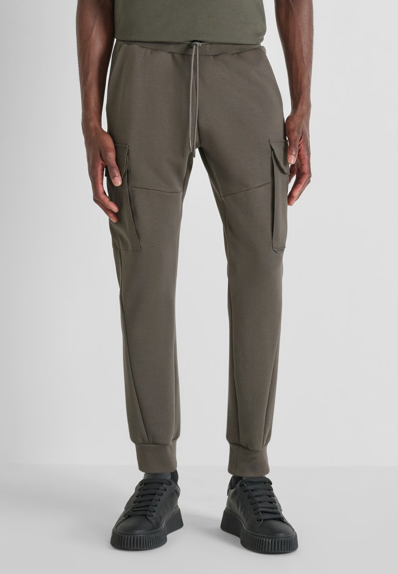 Olivgrüne Cargo-Hosen mit schmal zulaufendem Design, elastischem Bund mit Kordelzug und zwei Seitentaschen. Kombiniert mit schwarzen Sneakers.