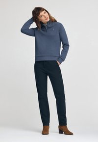 Marinblå sweatshirt med kvartdragkedja och ribbade ärmslut, matchad med mörka byxor och bruna mockaankelstövlar. Enkel, modern design.