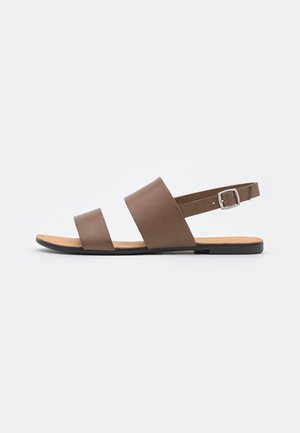 Flad brun sandal med to brede remme over foden og en justerbar spænde-rem rundt om hælen, på en lys baggrund.