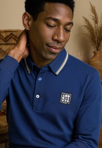 Marineblauw polo shirt met een kraag, twee knopen en een logo patch. Beschikt over een contrasterende gestreepte kraag en een textuurstof.