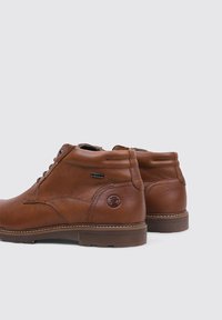 Braune Leder-Stiefeletten mit runder Zehenpartie, Schnürung vorne, Metallösen und einer Logo-Akzentuierung an der Ferse. Sichtbare genähte Sohlendetails.
