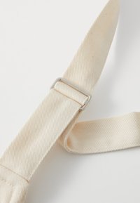 Kattunrem i myk beige med en teksturert diagonalvev. Har en silver rektangulær metalspenne for justerbar lengde.