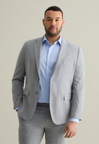Traje gris de rayas diplomáticas con solapas de muesca, bolsillos frontales y botones. Camisa de dress azul claro, de tela suave, ajuste entallado. Fondo neutral.