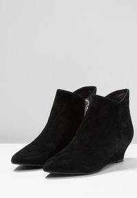 Bottes basses en daim noir avec un bout pointu et un talon compensé. Dotées d'une fermeture éclair latérale et d'une texture lisse, offrant une silhouette élégante.