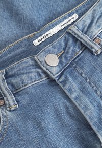 Světle modré džínové kalhoty s viditelným pasem, kovovým knoflíkem a štítkem s nápisem "GABBA". Vyznačují se vyblednutím a texturovanou látkou.