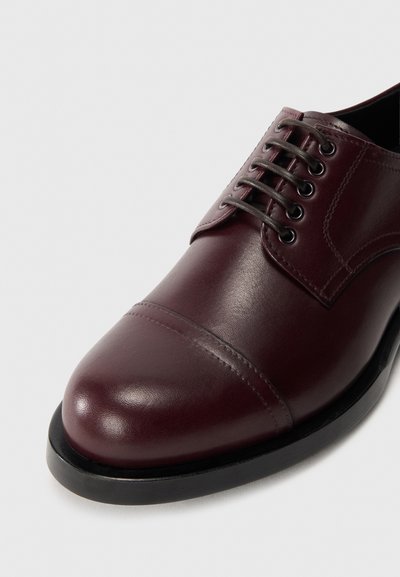 Scarpe eleganti in pelle bordeaux con finitura liscia, punta arrotondata, design a punta sagomata e lacci neri. Presenta una suola nera robusta.