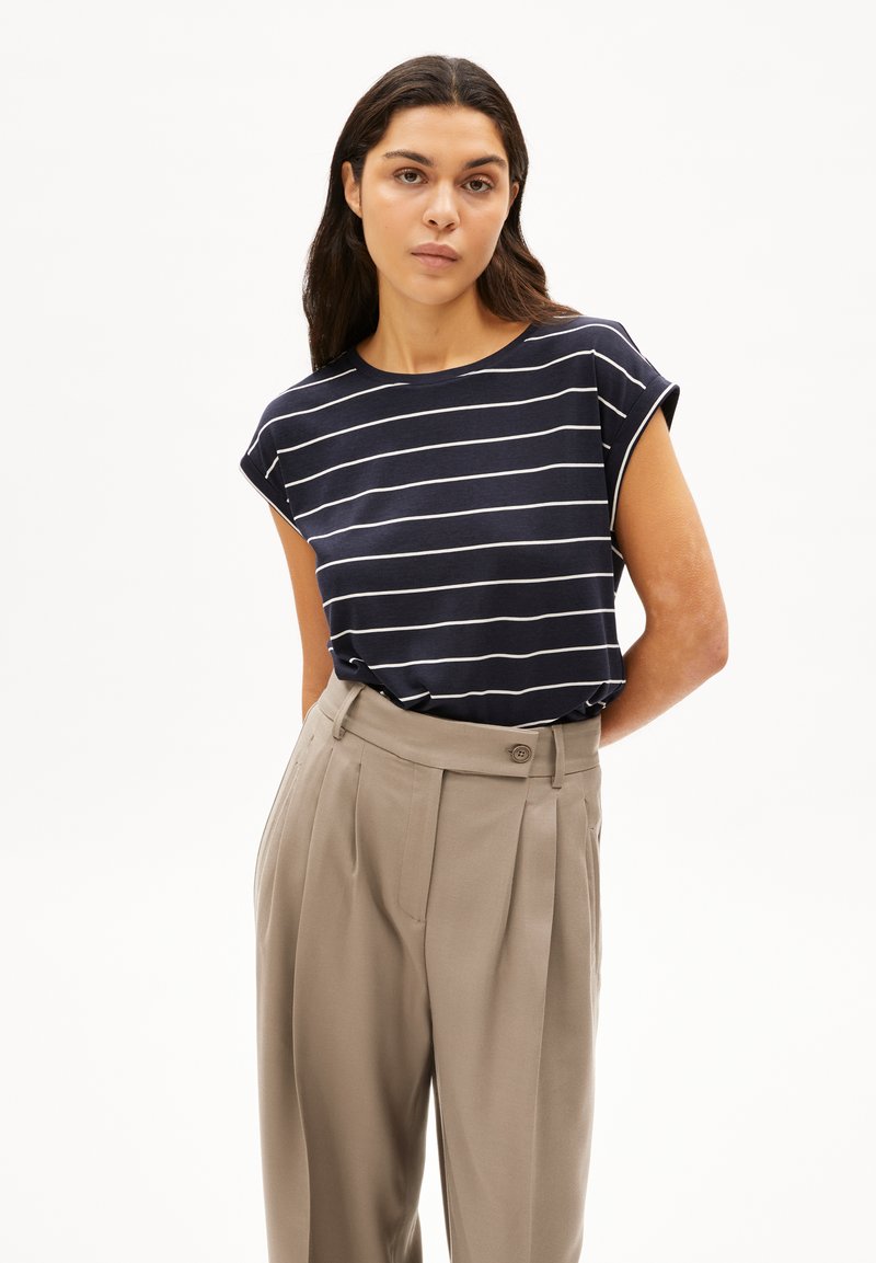 Navy striped T-shirt with rolled sleeves, paired with high-waisted beige pleated trousers featuring a button closure and side pockets.